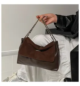 Detail of a brown leather shoulder bag featuring matte texture and a sleek metal chain strap