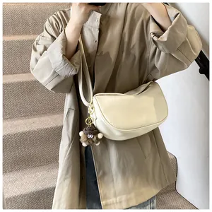 Detail of a beige leather saddle bag with a plush doll charm on a khaki trench coat