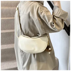 Detail of cream half-moon crossbody bag with leather texture and brown plush pendant