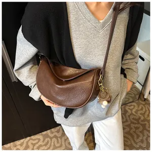 Detail of a dark brown half-moon crossbody bag with a fuzzy white ball charm accessory