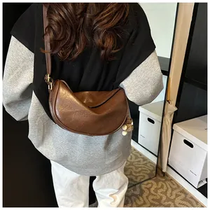 Brown leather half-moon shoulder bag shown from a rear angle on a model in a minimalist room