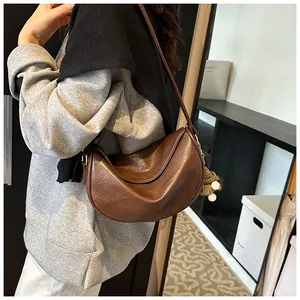 Detail view of a vintage brown half-moon shoulder bag with fuzzy ball charm accessory