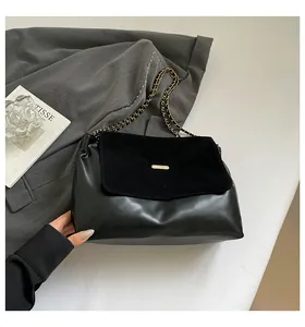 Detail of black leather handbag with suede flap, gold chain strap and metal hardware