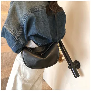 Chic black half-moon crossbody bag with decorative fur ball charm shown on a model