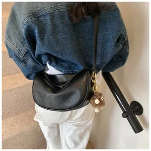 Detail of black half-moon hobo bag with plush charm on a model in a casual staircase setting