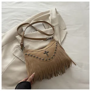 Close-up of suede crossbody bag with vintage rivets, cross pendant, and long fringe details
