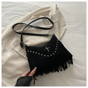 Detail of a black punk handbag with metal rivets, tassels, and a cross charm on a blazer