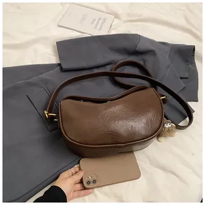 Close-up of a brown leather dumpling bag on a grey blazer with a plush monster charm