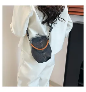 Detail of denim shell bag with orange handle and white stitching on a white blazer