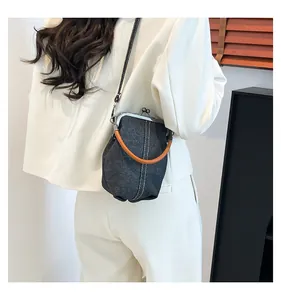 Detail of vintage denim shell bag featuring white stitching and orange handles worn by model