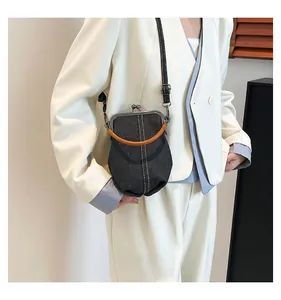 Detail of denim shell bag with orange handle and white stitching on a white blazer