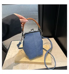 Macro detail of blue denim shell bag showing white stitching and brown handle accents