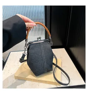Detail of a denim shell bag with white stitching and leather handle on a stone background