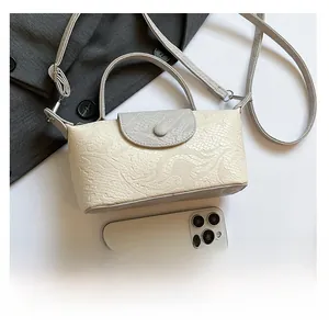 Mini cream and grey crossbody bag size comparison with a smartphone on grey blazer