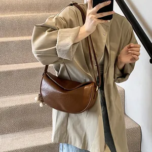 Retro brown half-moon shoulder bag with plush pearl charm on a stylish model