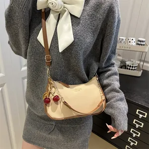 Chic beige textured leather crossbody bag with chain strap and cherry charm on model