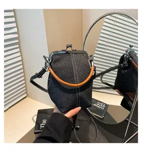Detailed macro shot of vintage denim kiss-lock bag with white contrast stitching and brown handle