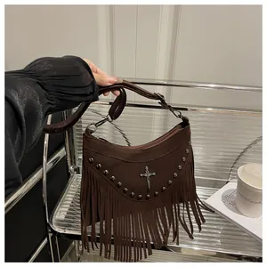 Detail view of brown suede crescent bag with silver rivets, cross charm and long fringes