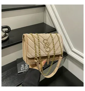 Détail d'un sac bandoulière en velours beige avec matelassage en V et pompon doré
