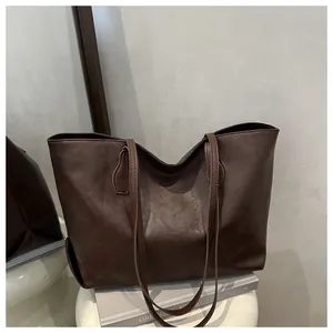 Detailed side view of deep brown vintage tote bag with slim straps on white pedestal