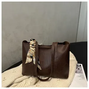 Detail der dunkelbraunen Leder-Tote-Bag mit Seidenschal auf weißem Strickhintergrund