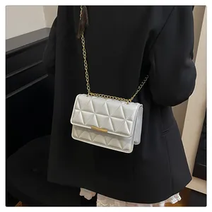 Close-up of white quilted crossbody bag with gold chain strap on a black blazer