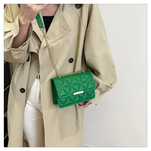 Detail view of green quilted crossbody bag with gold chain strap on a trench coat