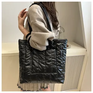 Detailed view of black quilted tote bag texture and glossy shoulder strap detail