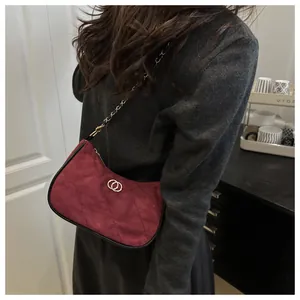 Detail of burgundy quilted suede shoulder bag with gold chain strap on a model