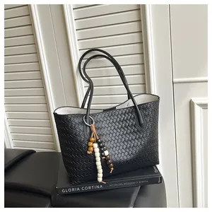 Detail of black woven leather tote bag featuring a wooden bead pendant and interior liner