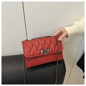 Detail of red quilted crossbody bag with gunmetal lock and punk style chain decor
