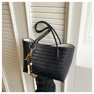Detail of black woven leather tote bag with colorful beaded tassel and slim handles