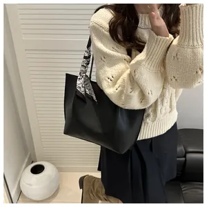 Detail of black pleated tote bag with marble pattern scarf on a leather sofa