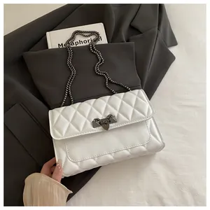 Detailed view of white quilted crossbody bag with gunmetal chain on a gray blazer