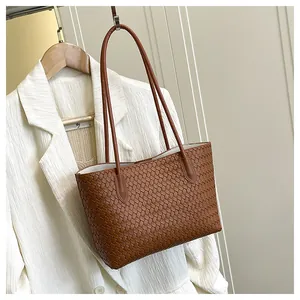 Detail of woven brown tote bag on a white suit hanger against a beige wall