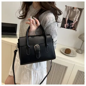 Close-up of black leather handbag with round handles and metal buckle on a desk