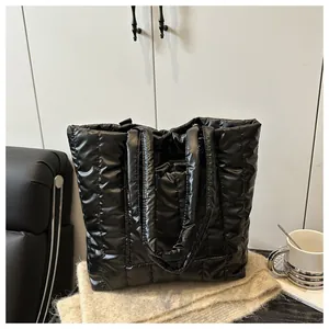Close-up of the glossy quilted surface and wide handles of the black puffy tote bag
