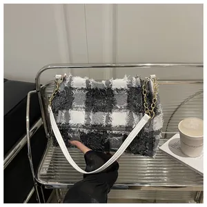 Detail of tweed checkered handbag with gold chain and white leather strap on metal rack