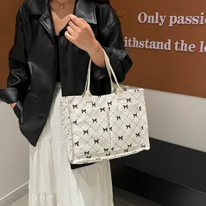 Cream corduroy quilted tote bag with black bows worn over shoulder in casual style