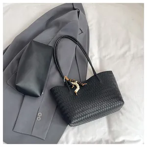 Flat lay of woven leather tote bag with small pouch and beaded charm on gray suit