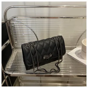 Detail of black quilted leather shoulder bag with geometric metal lock and chain strap