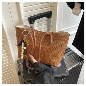 Detail of a brown woven leather tote bag with wooden bead tassel on a silver suitcase