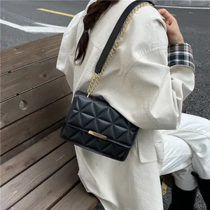 Quilted black crossbody bag with gold chain strap on stylish beige coat