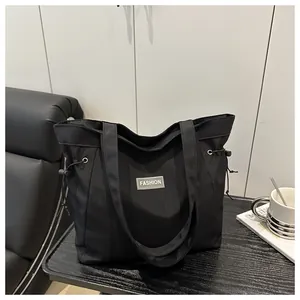 Detail of a black large-capacity tote bag with side drawstrings and FASHION label