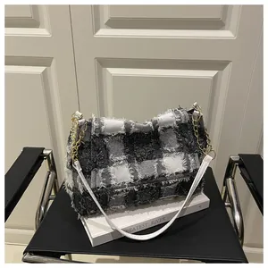 Detail view of the black and white plaid handbag with fringe edges and gold chain strap