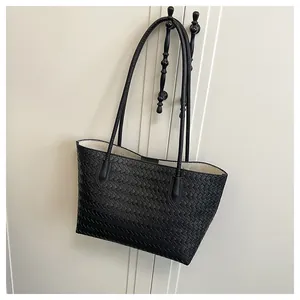 Detail shot of black woven tote bag texture with long straps on a minimalist background