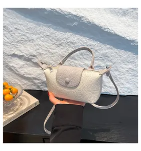 Detail showing the embossed texture of the mini beige crossbody bag on a textured surface