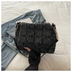 Detailed top view of black fringed texture handbag with gold chain and blue denim jacket