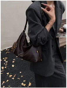 Detail of a dark brown crescent bag with a heart-shaped leopard print charm and a gold emblem