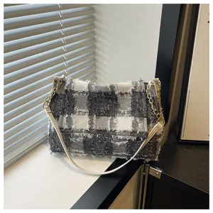Detailed view of plaid handbag with frayed edges and golden chain on a minimalist window
